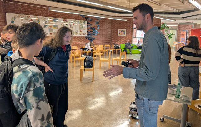 Menschen im Gespräch in einem modernen Schulraum mit Holzmöbeln und Pflanzen.